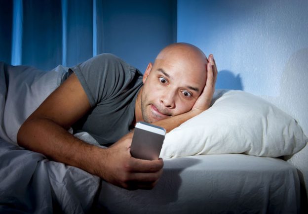 Bald Man Lying in Bed Looking at his Smart Phone Late at Night